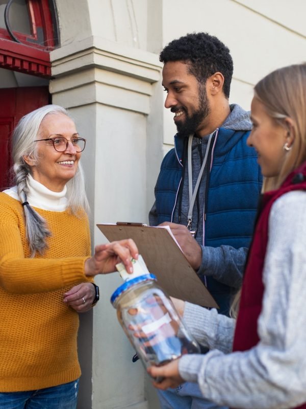 young-door-to-door-fundraisers-talking-to-senior-woman-and-collecting-money-for-charity-in-street.jpg